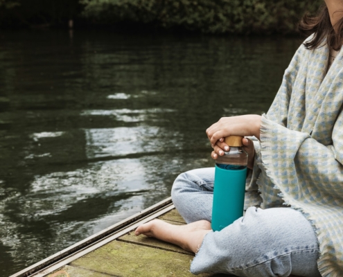 woman in gray sweater and gray pants sitting on brown wooden boat on river during daytime