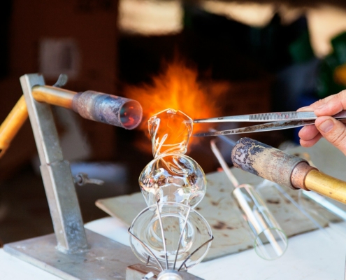 person molding glass vase through blowtorch